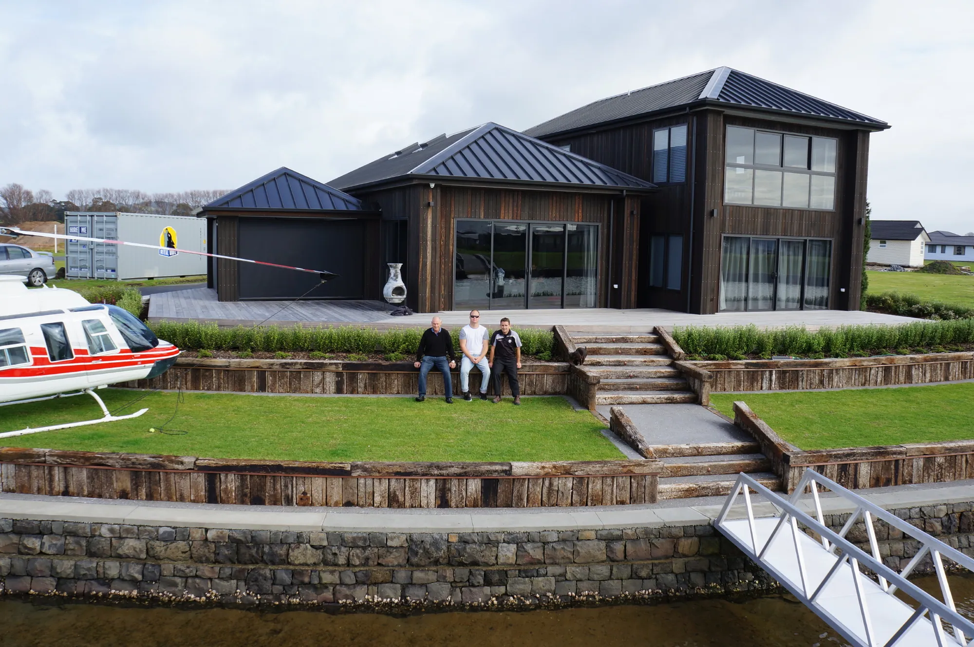 Dark-clad two-storey canal home with a stone retaining wall and gangway to the water