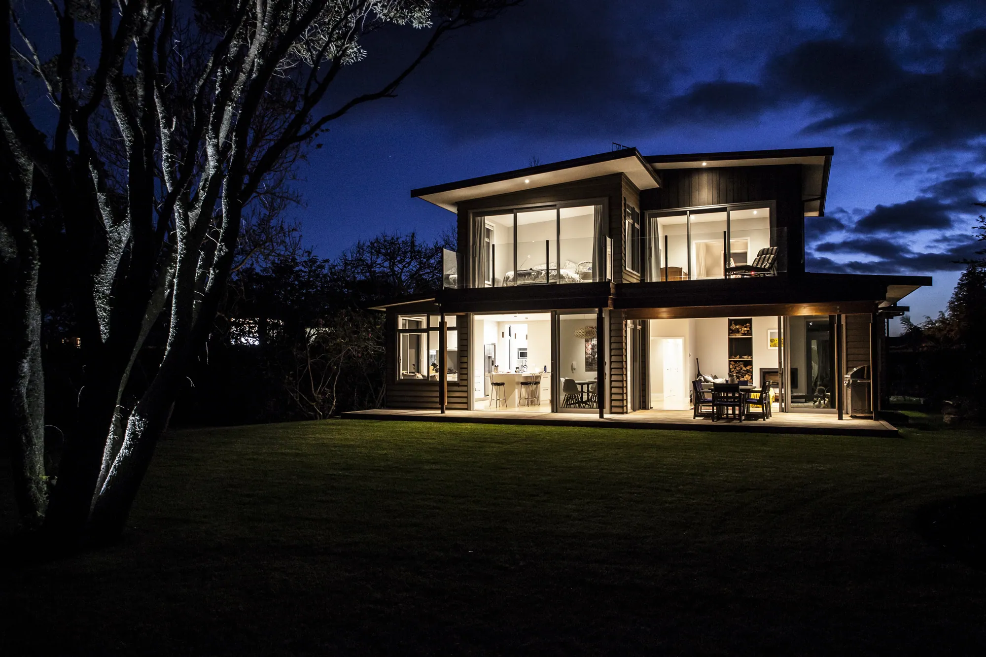 Two-storey home lit from within at night, seen across the lawn