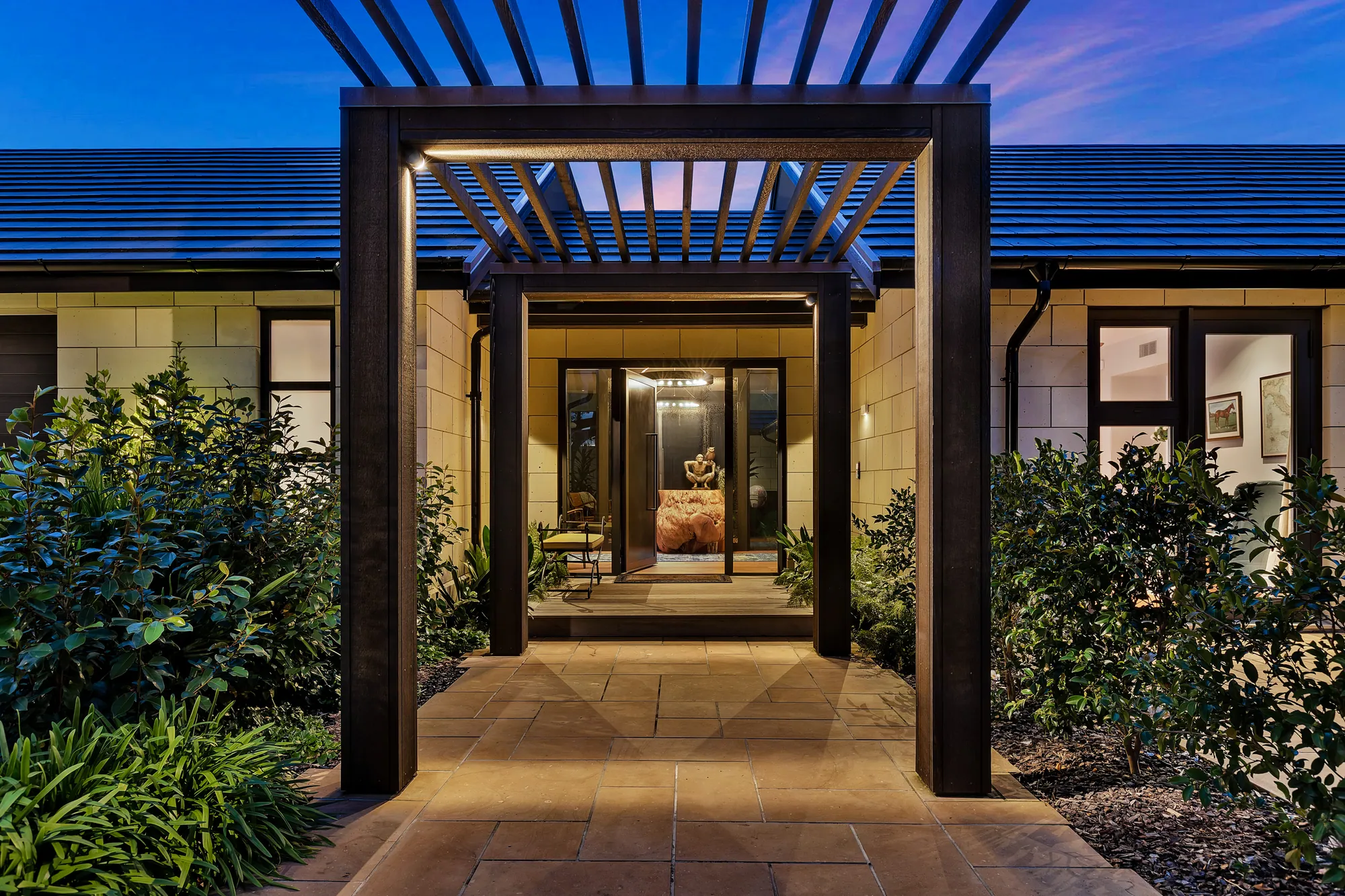 Lit pergola entry to a custom Cogan home at dusk