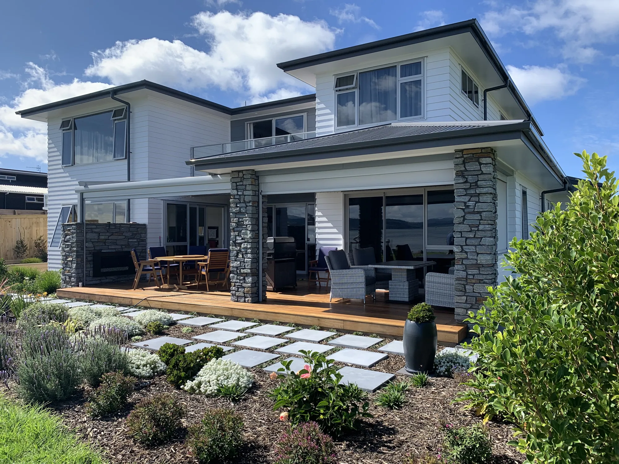 Two-storey weatherboard home with schist columns and a covered deck