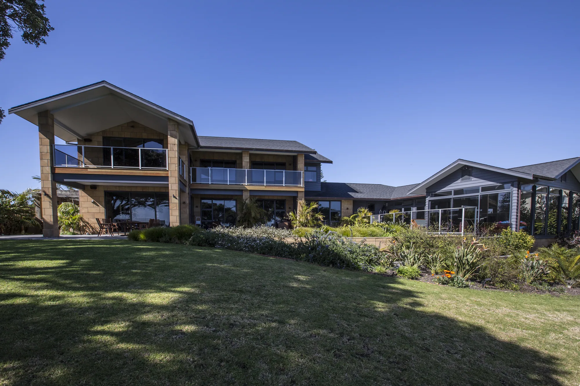 Two-storey home with a gabled entry and glass balconies, seen across the lawn