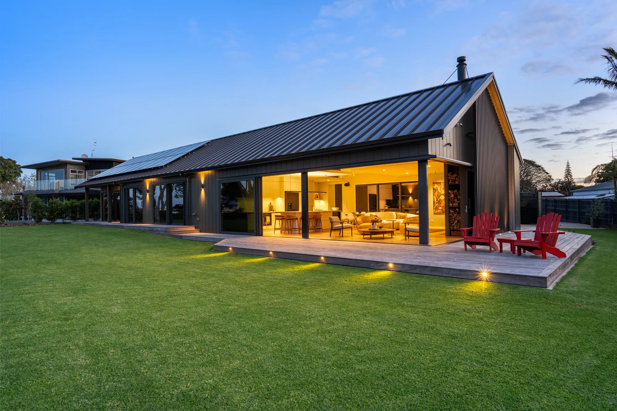 The Cogan waterfront showhome at dusk, lit from within, seen across the lawn